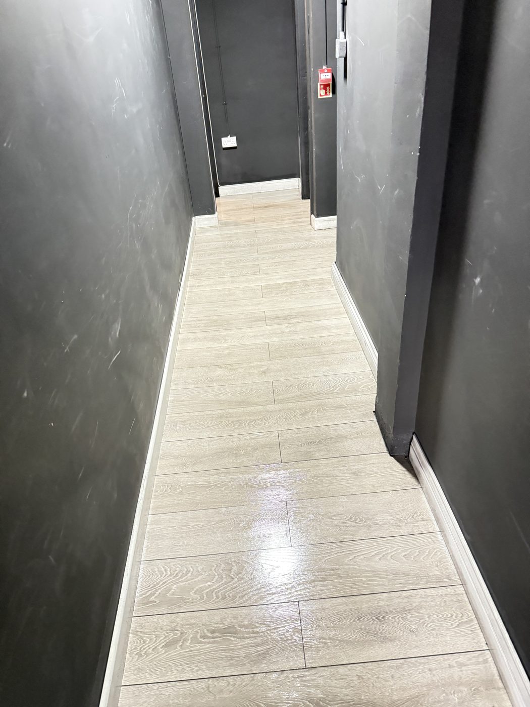 A clean corridor with pale wood effect flooring in a shared building cleaned by Cadence Clean