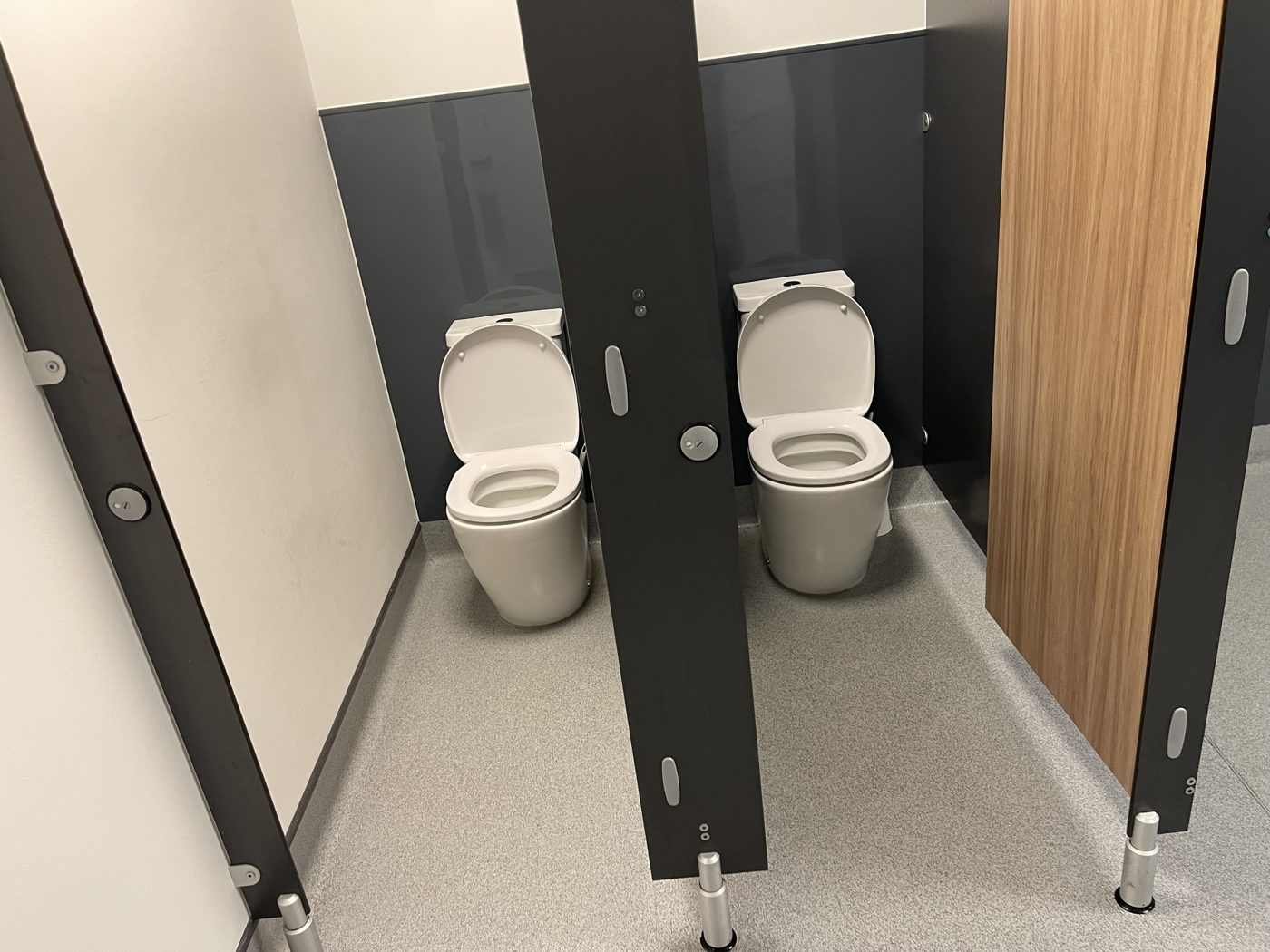 Clean staff toilet cubicles with dark partitions at an office cleaned by Cadence Clean