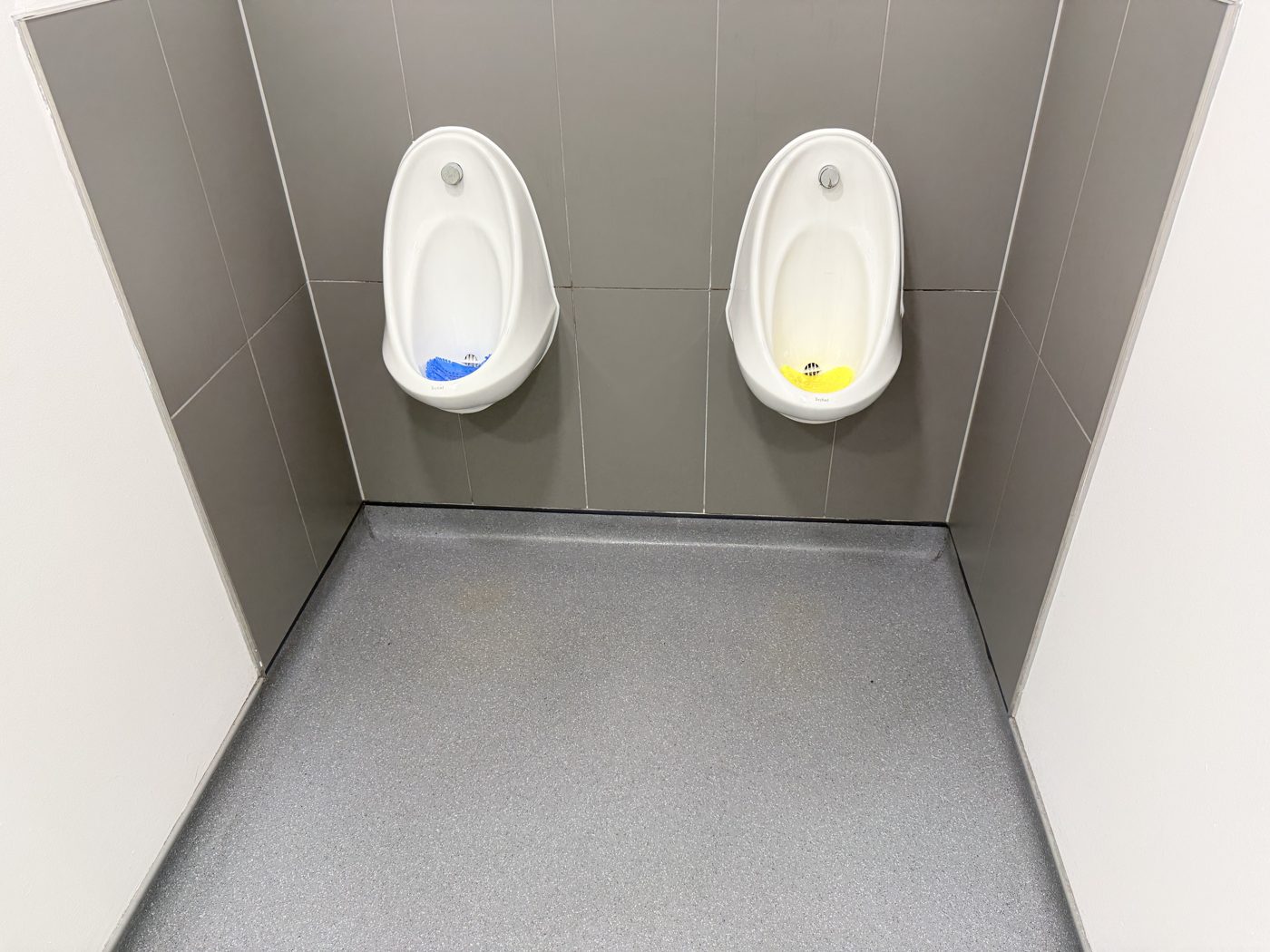 Clean urinals on a grey tiled wall at a commercial premises cleaned by Cadence Clean